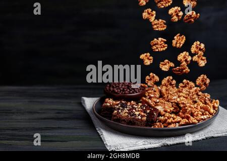 Le noci cadono in un piatto con pezzi di cioccolato brownie e noci- concetto per cibo sano durante la quarantena domestica Foto Stock