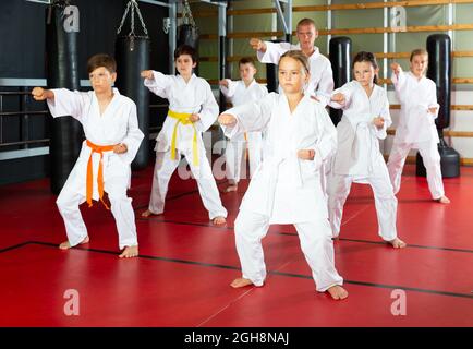 I bambini Karate in kimono che eseguono il kata si muovono con il loro insegnante in palestra durante l'allenamento di gruppo. Foto Stock