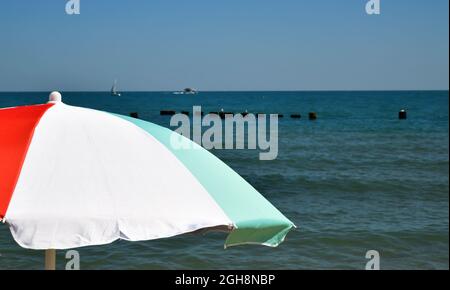 ombrello colorato contro il cielo blu estivo lungo la spiaggia Foto Stock