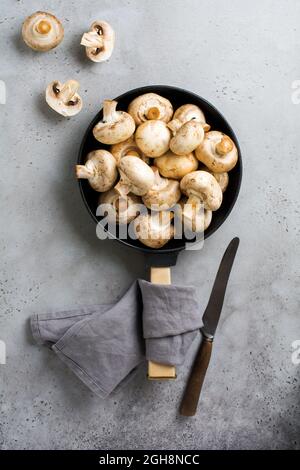 Funghi crudi champignon in ghisa vecchia padella su un vecchio cemento grigio fondo rustico per la frittura. Vista dall'alto Foto Stock