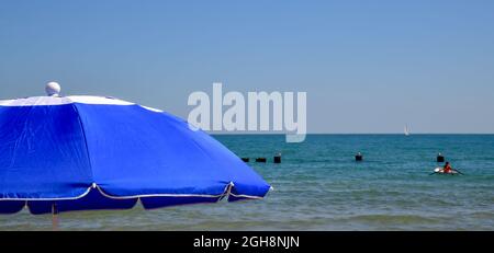 ombrello colorato contro il cielo blu estivo lungo la spiaggia Foto Stock