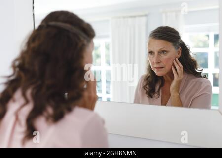 Donna caucasica anziana in bagno, guardando il suo volto a specchio. Stile di vita pensionamento e il processo di invecchiamento. Foto Stock