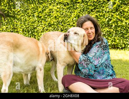 Donna matura felice con i cani Labrador Retriever in giardino. Foto Stock