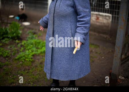 Nonna in un vecchio cappotto. Una donna si trova sulla strada. Una vecchia donna in Russia nutriva gatti. Foto Stock