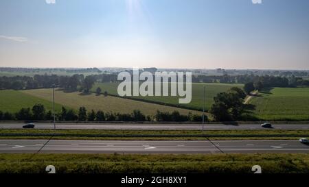 Vista aerea della strada tra campi agricoli e piantagioni sotto un cielo azzurro chiaro, fucilato con un drone. Foto di alta qualità Foto Stock