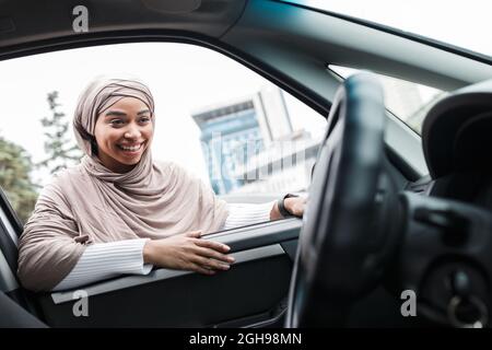 Felice attraente musulmano afro americano donna acquirente guarda in salone di nuova auto da finestra aperta Foto Stock