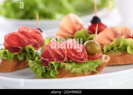 Tartine di baguette tenue con lattuga, salame o prosciutto di Parma, pomodori, mozzarella e olive. Piatto assortito di prelibatezze per la festa. Foto Stock