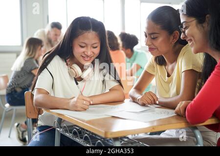 Studenti in classe che fanno un progetto di squadra seduti insieme in classe. Asiatico, caucasico e Latina. Foto Stock