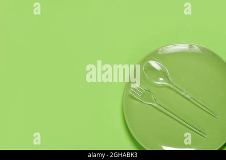 Piatto verde e forchetta in plastica con cucchiaio su sfondo verde. Spazio di copia Foto Stock