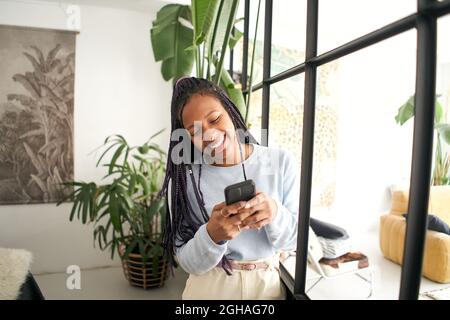 Giovane afroamericana che chiacchiera sul suo smartphone. Ragazza sorridente usando un telefono cellulare in un loft moderno. Foto Stock
