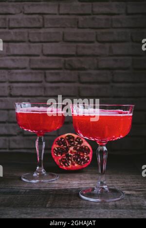 Cocktail 'Barbotage' a base di sciroppo di grenadina, succo d'arancia e vino frizzante, servito in bicchieri vintage champagne coupé, con metà di melograno. Foto Stock