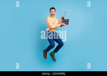 Foto del regista eccitato ragazzo salto filmato tenere clapper indossare braciere camicia isolato blu sfondo colore Foto Stock