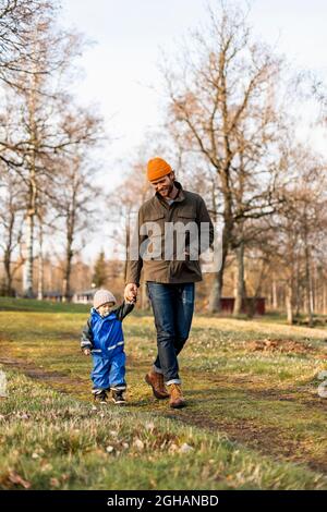 Tutta la lunghezza del padre e del figlio che tengono le mani mentre camminano insieme al parco Foto Stock