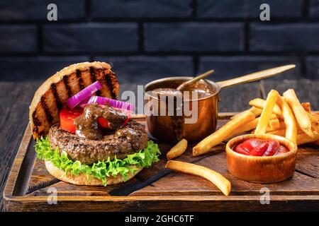 hamburger alla griglia di panna affettata con hamburger di manzo succoso, foglie di lattuga, pomodori, anelli di cipolla rossa e salsa barbeque condita su un tagliere Foto Stock