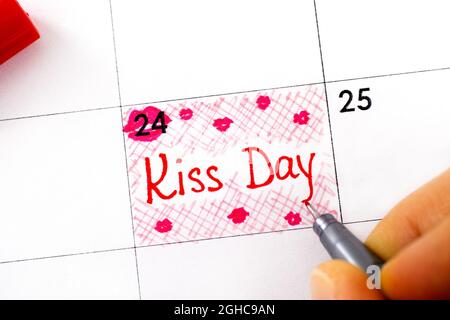 Una donna dita con una penna di scrittura promemoria Kiss giorno nel calendario. Settembre 24. Foto Stock