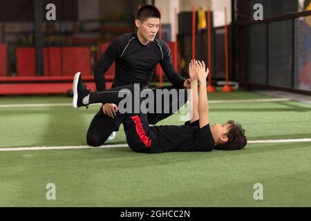 Ragazzino che ha una lezione di esercizi con allenatore in palestra Foto Stock