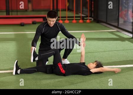 Ragazzino che ha una lezione di esercizi con allenatore in palestra Foto Stock