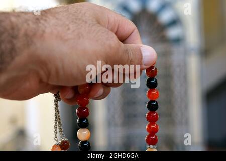 Una mano tiene un rosario islamico colorato su uno sfondo sfocato della moschea nicchia Mihrab, le perle di preghiera islamica chiamato Misbaha o Tasbih, preghiera Foto Stock