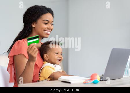 Sorridendo Donna Nera che tiene bambino e che fa lo shopping in linea a casa Foto Stock