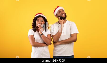 Sognanti sposi afroamericani in cappelli di santa tenendo le dita sui chins e pensando su sfondo giallo studio Foto Stock