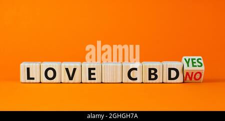 Love CBD, simbolo del cannabidiolo. Girò un cubo di legno e cambiò le parole "Love CBD no" in "Love CBD yes". Bellissimo sfondo arancione, spazio copia. Medico Foto Stock