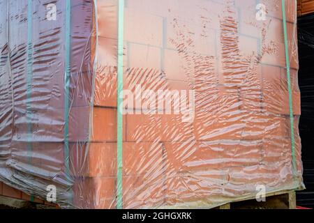 Mattoni rossi ricoperti di pellicola di imballaggio su pallet in un magazzino di materiali da costruzione. Foto Stock