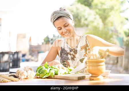 Bella giovane donna sta preparando il pranzo nella cucina all'aperto. Cibo sano. Vegan - concetto di Dieting. Stile di vita sano. Cucina a casa. Preparare Foo Foto Stock