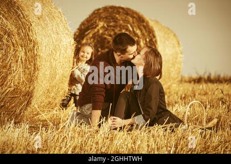 Felice famiglia giovane con bambina di due anni accanto a balle di fieno in campo raccolto Foto Stock