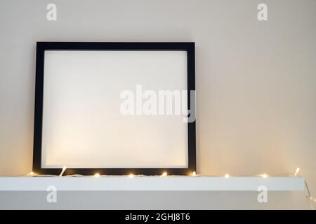 La cornice fotografica in legno bianco si trova all'interno su uno sfondo bianco. Primo piano della cornice del poster mockup nell'interno della casa. Foto Stock