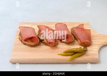 Sandwich con carne secca affettata servita su tagliere su sfondo grigio neutro Foto Stock