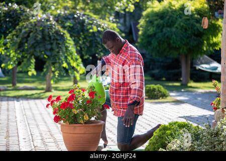 African american uomo che innaffiano fiore forma annaffiatura può in giardino. Concetto di hobby e lifestyle Foto Stock