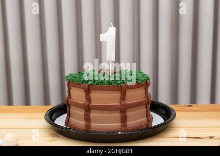 Torta al cioccolato decorata. Un anno di candela bianca su torta decorata in tema country su un tavolo di legno chiaro. Foto Stock