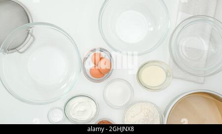 Ingredienti e piatti per fare la torta da vicino sul tavolo da cucina, vista dall'alto. Passo dopo passo ricetta torta al cioccolato, sfondo bianco tavolo da cucina Foto Stock