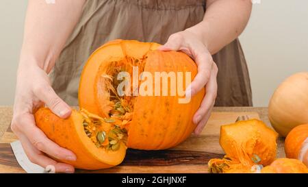 Donna taglia la zucca arancione in fette su tagliere di legno. Step by step purea di zucca ricetta, stile di vita Foto Stock