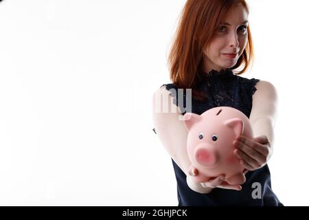 Giovane donna che tiene una banca piggy esteso alla macchina fotografica con un sorriso di soddisfazione in un concetto di risparmio e di investimento o finanziario Foto Stock