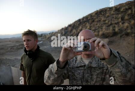 Il personale dell'esercito degli Stati Uniti Sgt. Jason Loomis, di Los Angeles, California, si prepara a fotografare i giri di artiglieria da 155 mm che hanno un impatto su una collina vicina a Combat Outpost Cherkatah, provincia di Khowst, Afghanistan, 26 novembre 2009. L'artiglieria è stata sparata dalle forze statunitensi dalla base operativa Forward Salerno durante un incendio di prova. Foto Stock