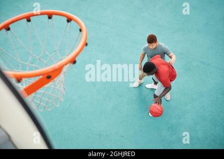 Direttamente sopra la vista del padre nero dribbling palla mentre combattendo con figlio per esso sotto l'anello su campo sportivo Foto Stock