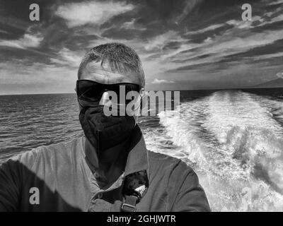 Foto in scala di grigi di un uomo di mezza età dall'Italia che prende un selfie che indossa una maschera sanitaria al mare Foto Stock