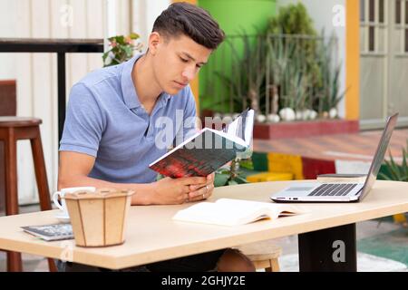 Latino e molto attraente uomo che legge all'aperto su un banco di studio Foto Stock