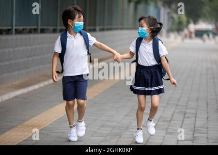 Due alunni che indossano maschere chirurgiche per andare a scuola Foto Stock