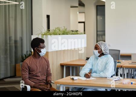 Infermiere medico in tuta protettiva e maschera medica che parla con il paziente prima di poter ottenere il vaccino contro COVID-19 Foto Stock