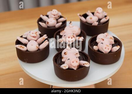 Vassoio bianco con caramelle decorate, simpatici maialini rosa che giocano nel fango di marzapane e cioccolato. Messa a fuoco selettiva. Piccoli maiali che si divertono in Foto Stock