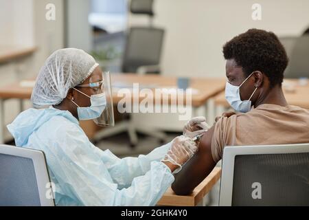 Spaventato il giovane uomo nero che chiude gli occhi quando ottiene il colpo di vaccino contro il coronavirus Foto Stock