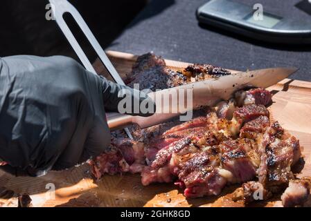 Mano guanto di uno chef che intagliano una porzione di carne di prima costola grigliata dal barbecue su un tagliere di legno in un primo piano sul cibo Foto Stock