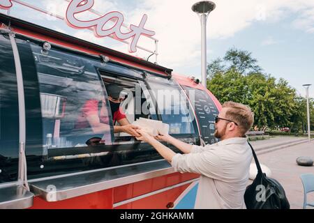 Giovane uomo occupato che acquista fast food in camion rosso strada in ambiente urbano Foto Stock