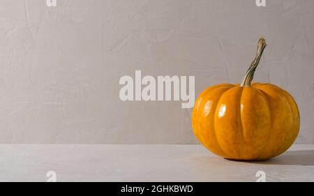 Minimalismo sfondo autunnale - zucca arancione su sfondo beige. Sfondo vuoto per la dimostrazione di bevande, cibo, prodotti con copia del testo Foto Stock