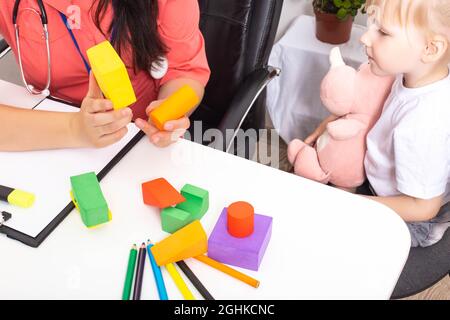 Il medico mostra le figure multicolore del costruttore ad una bambina di 3-4 anni. Sviluppo del pensiero e della logica nei bambini Foto Stock