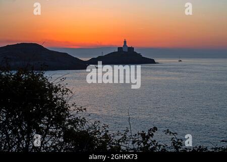 Swansea, Regno Unito. 07 settembre 2021. Una piccola barca a vela passa accanto al faro Mumbles illuminato vicino Swansea, mentre la nebbia marina inizia a sgorgare all'alba presto questa mattina all'inizio di una splendida giornata d'autunno. Credit: Phil Rees/Alamy Live News Foto Stock