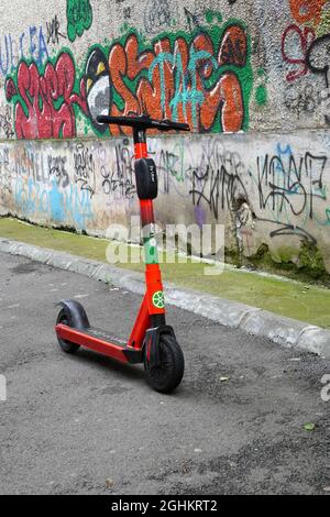 BUCAREST, ROMANIA - 22 giugno 2021: Scooter elettrico nolizzabile del marchio Lime di Uber, a sinistra di fronte al colorato muro di graffiti Foto Stock
