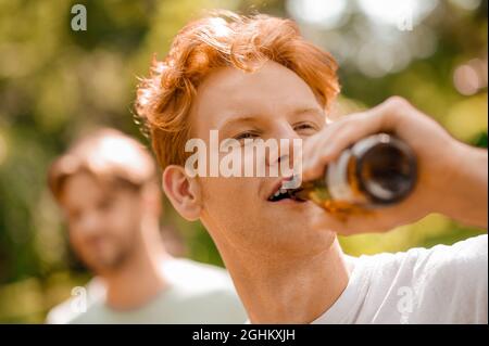 Red head ragazzo bere da bottiglia godendo momento Foto Stock